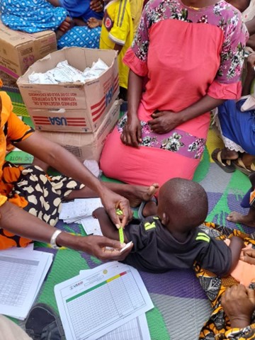 Women in Mauritania in brightly dressed clothing measuring the arm of a small child in order to assess if they are at risk of malnutrition.